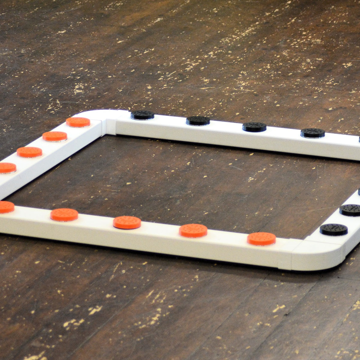 A white sniffer dog system with orange and black vented metal pots and connectors on a wooden floor.